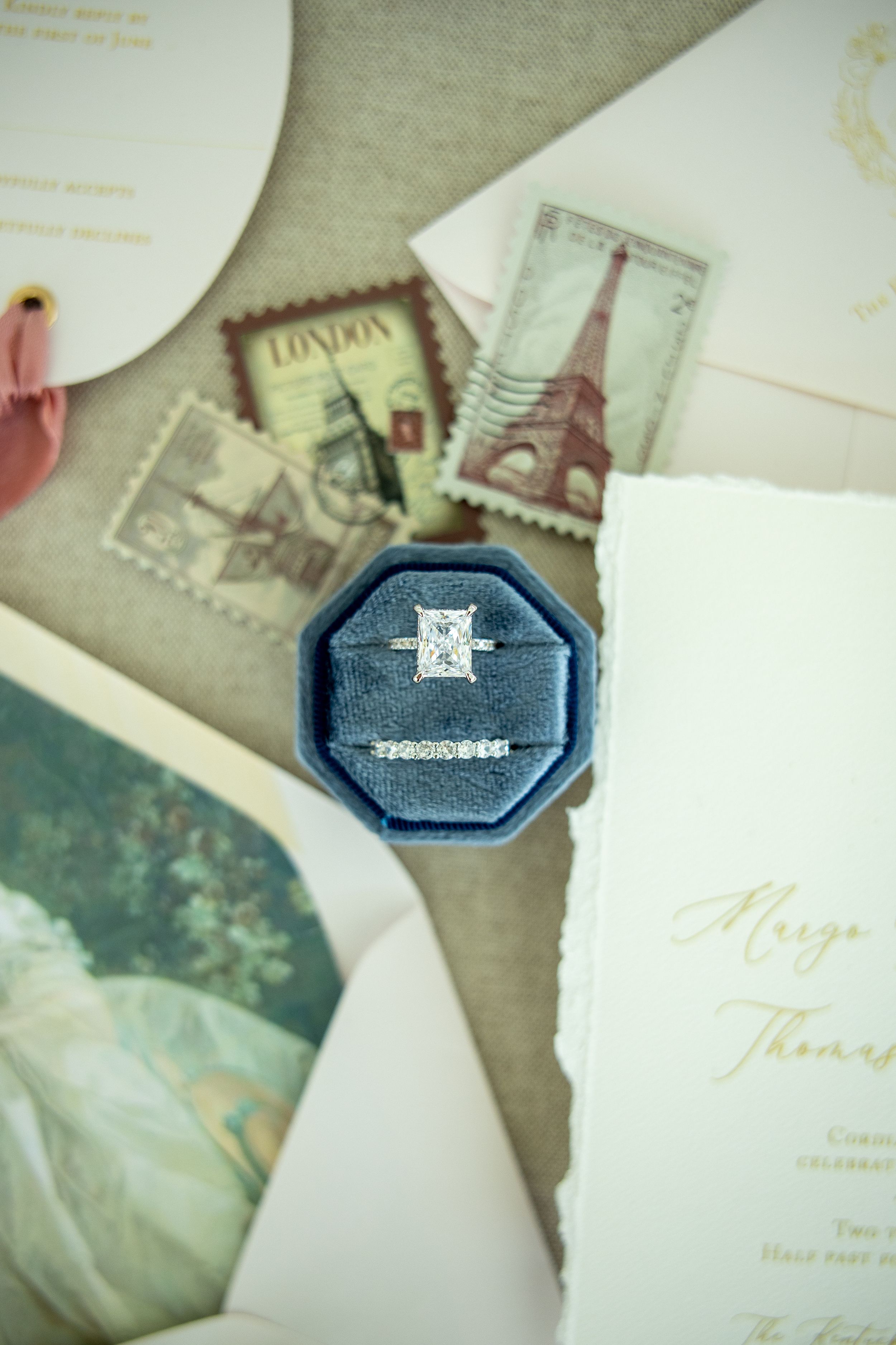 Diamond engagement ring and wedding band in blue velvet box with vintage travel stamps.