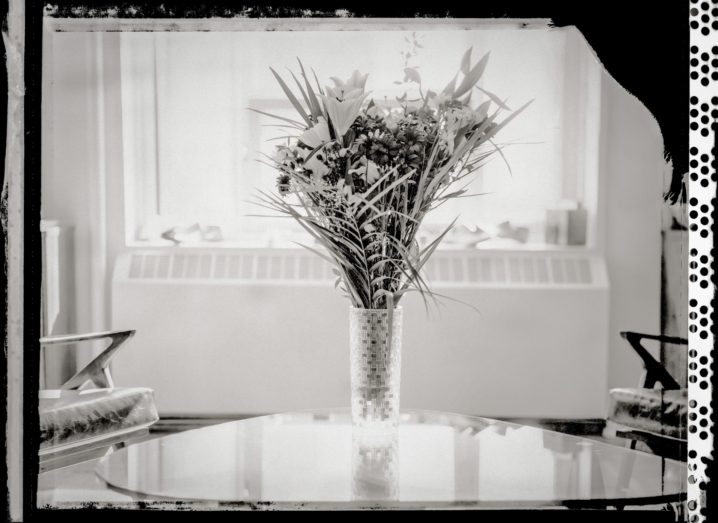 Black and white photo of a floral arrangement in a crystal vase on a glass table near a window.
