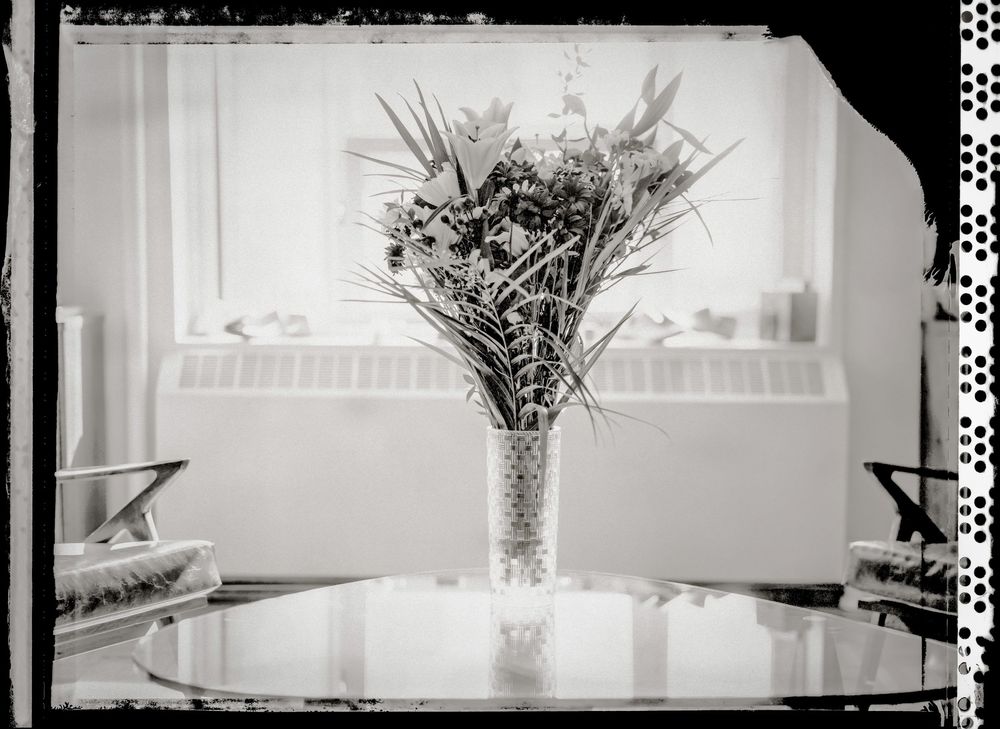 Black and white photo of a floral arrangement in a crystal vase on a glass table near a window.