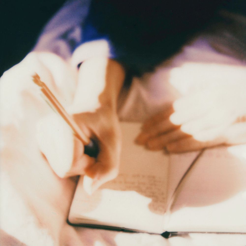 A person writing in a notebook with a pen, captured in a soft, dreamy, blurred artistic style.