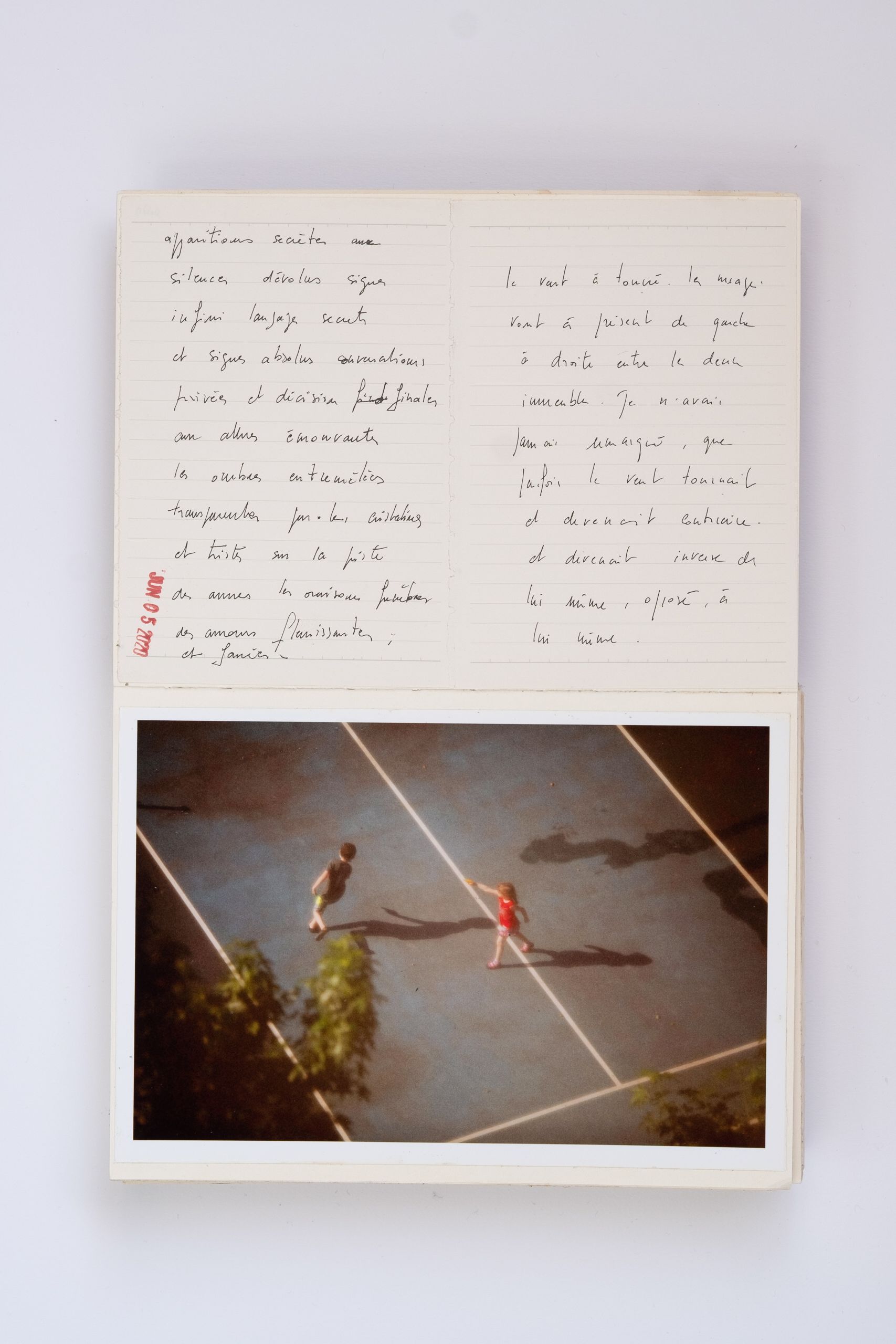 Open notebook with French handwritten text beside a vintage photo of two figures on a tennis court.