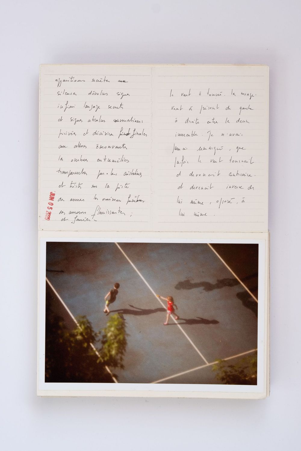 Open notebook with French handwritten text beside a vintage photo of two figures on a tennis court.