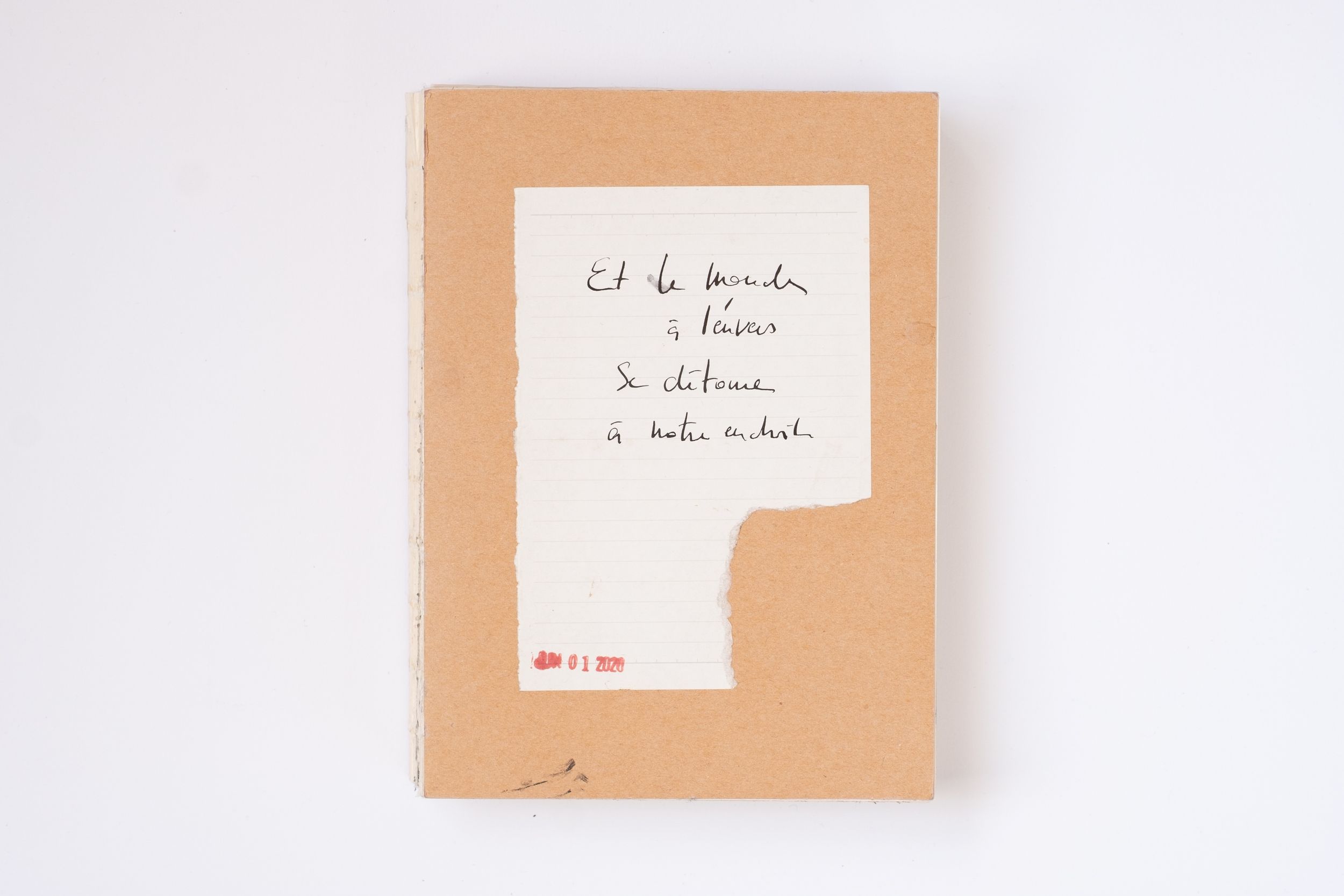 Handwritten French text on white paper attached to a kraft cardboard notebook cover with a red stamp.