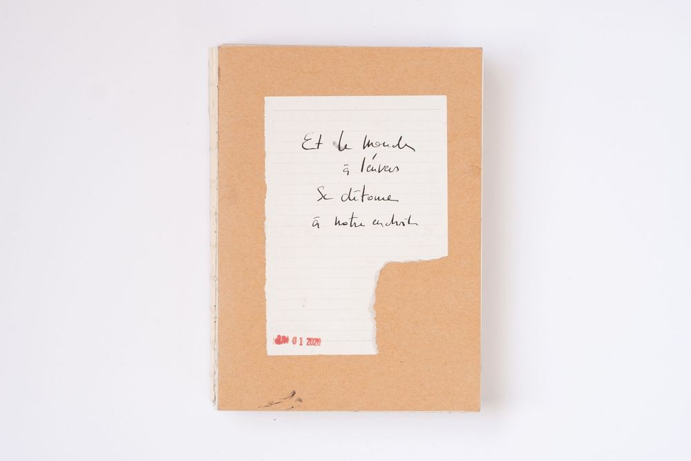 Handwritten French text on white paper attached to a kraft cardboard notebook cover with a red stamp.