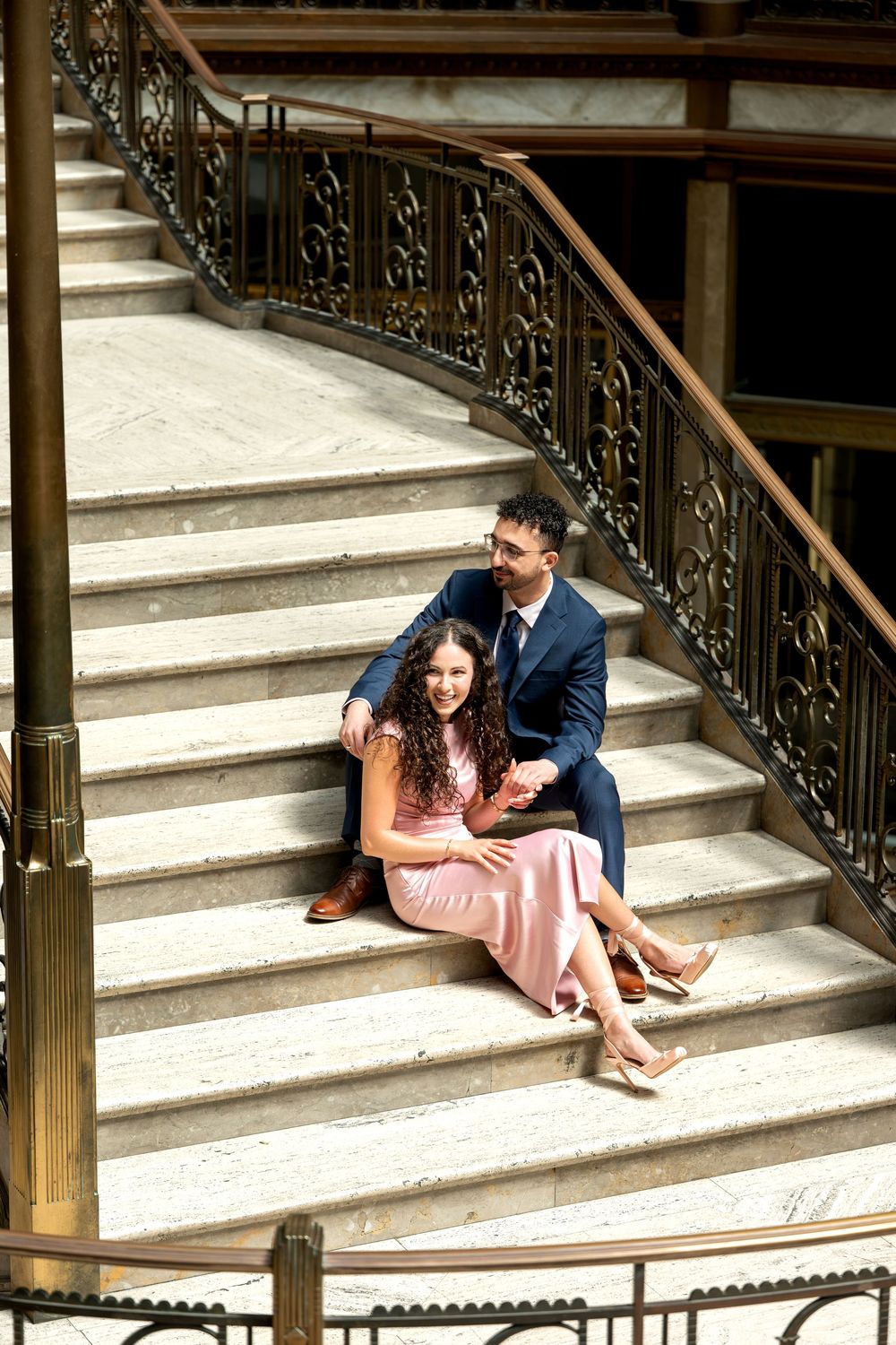 Couple sitting on marble stairs with ornate iron railing in elegant venue.