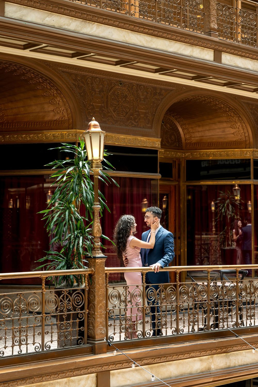 Romantic couple in formal attire sharing a tender moment on an ornate golden balcony.
