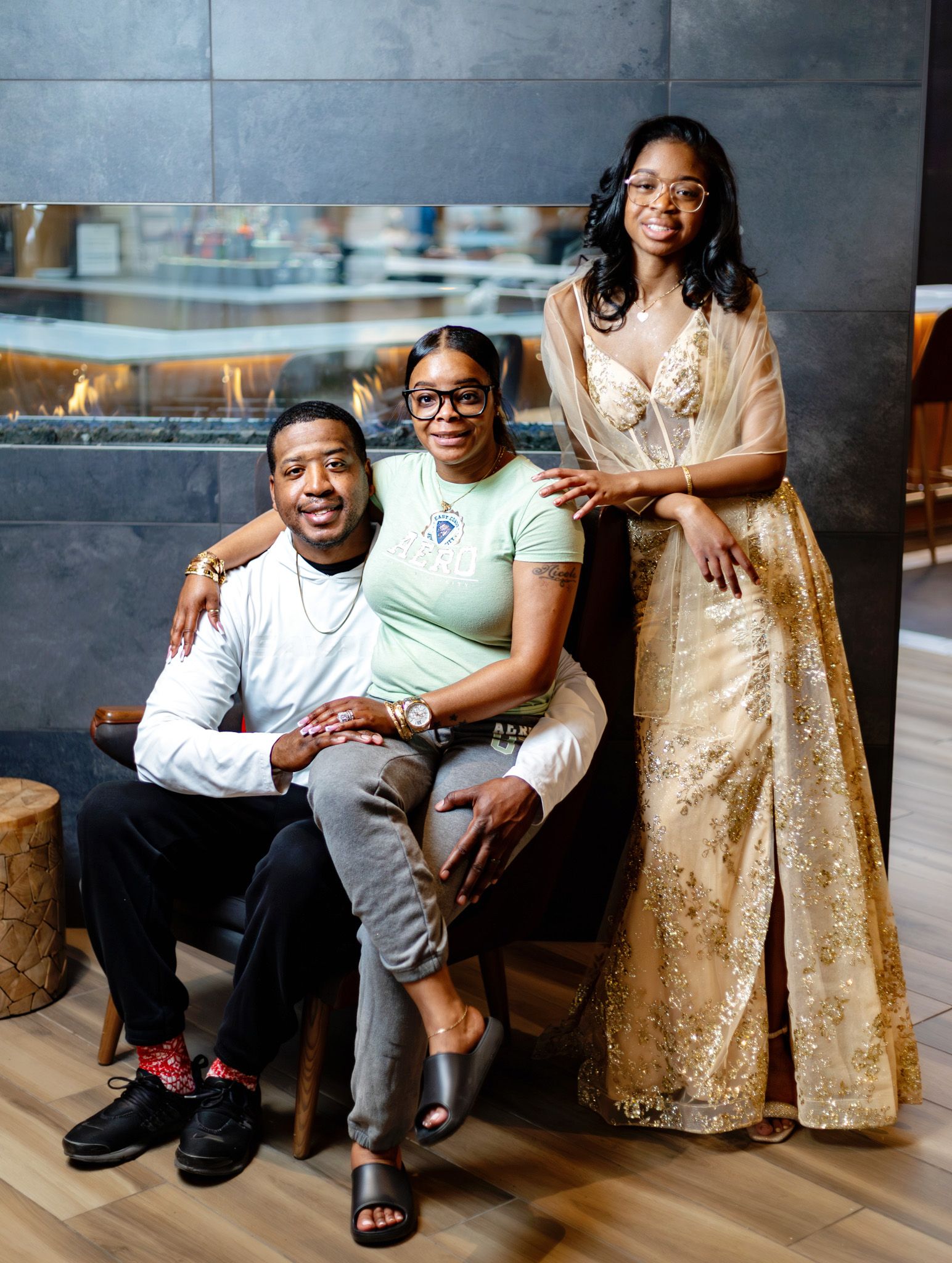 Three stylish people pose together in a modern venue, wearing elegant outfits including a gold gown and casual chic attire.