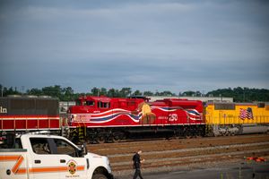 Red locomotive engine 250 with decorative graphics at a rail yard, with a white truck and worker nearby.