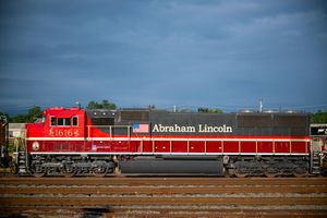 Red and gray Abraham Lincoln locomotive train engine on railroad tracks under cloudy sky.