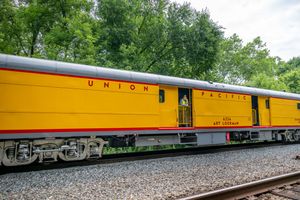 Bright yellow Union Pacific passenger train car with a person standing in the doorway, surrounded by lush green trees.