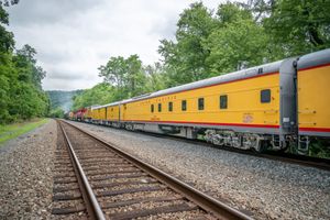 Yellow Union Pacific passenger train cars traveling along railroad tracks surrounded by lush green trees.