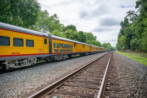 Yellow Union Pacific passenger train traveling through lush green countryside on a sunny day.