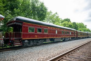 Vintage red Northern railroad passenger car on tracks surrounded by lush green trees on a sunny day.