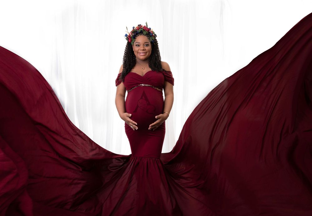 Dramatic maternity photo featuring flowing burgundy dress with billowing fabric against white background.