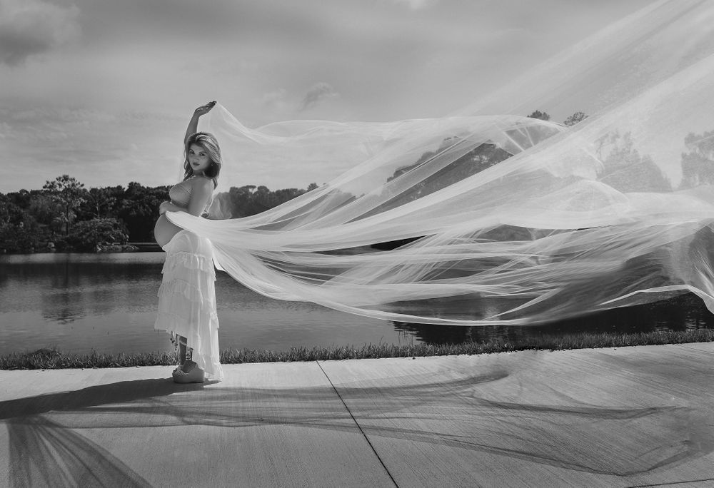 Dramatic black and white photo of flowing bridal veil caught in wind by lake.