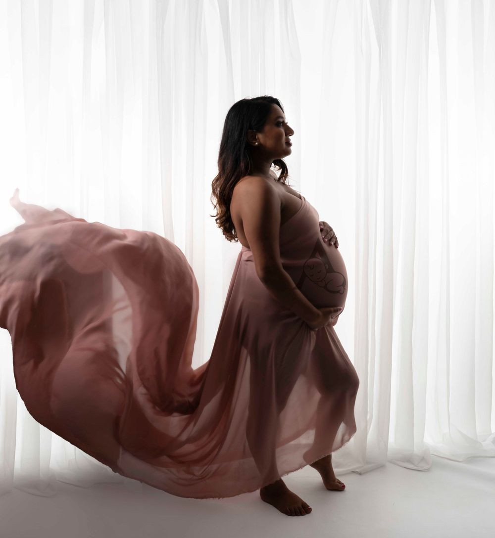 Silhouette of pregnant woman in flowing dusty rose dress against white background.