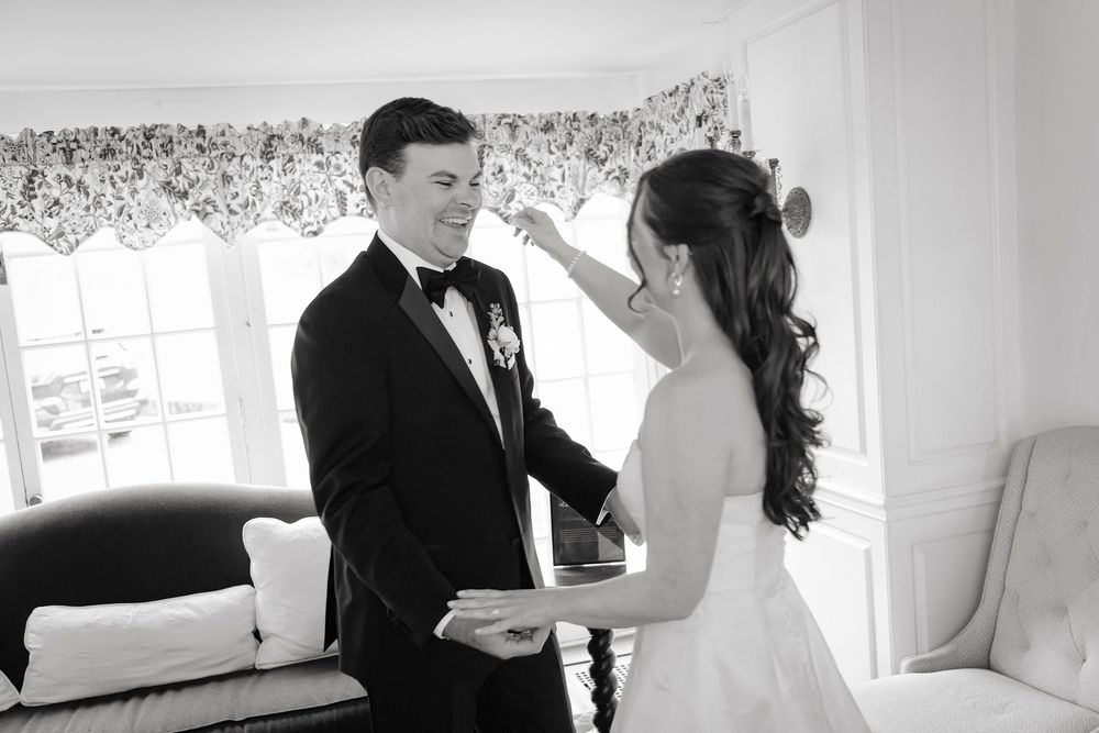Black and white photo of a bride and groom sharing a tender moment, smiling at each other in an elegant room.