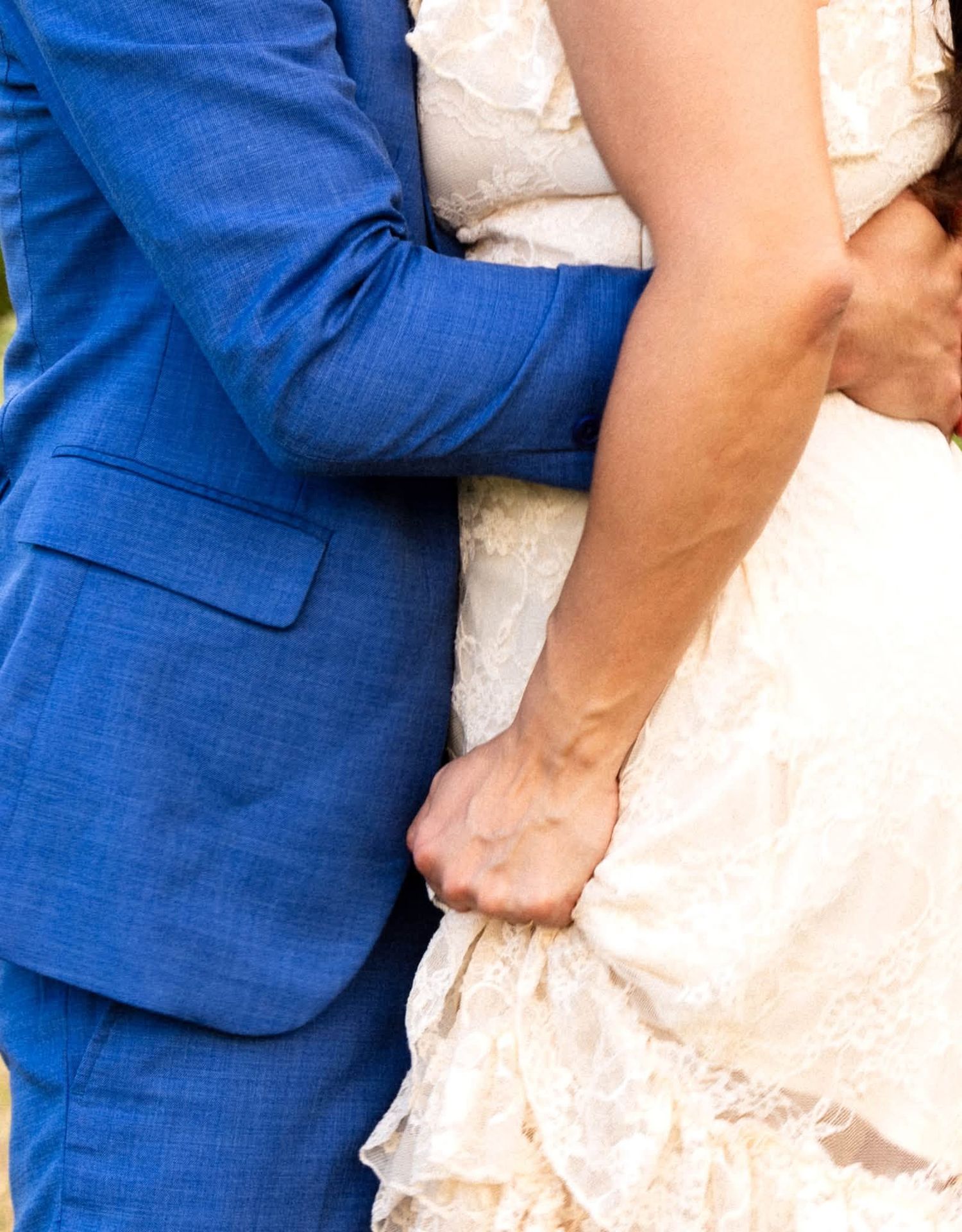 A bride in a white dress and groom in a blue suit walk hand-in-hand through a golden grassy meadow.