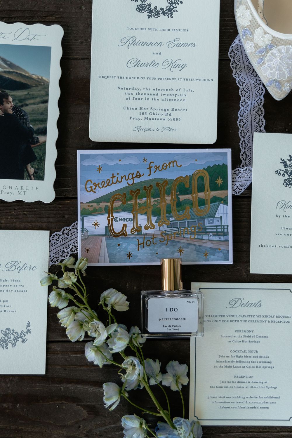 Elegant wedding invitation suite with floral details, perfume bottle, and a Chico Hot Springs postcard on rustic wood.