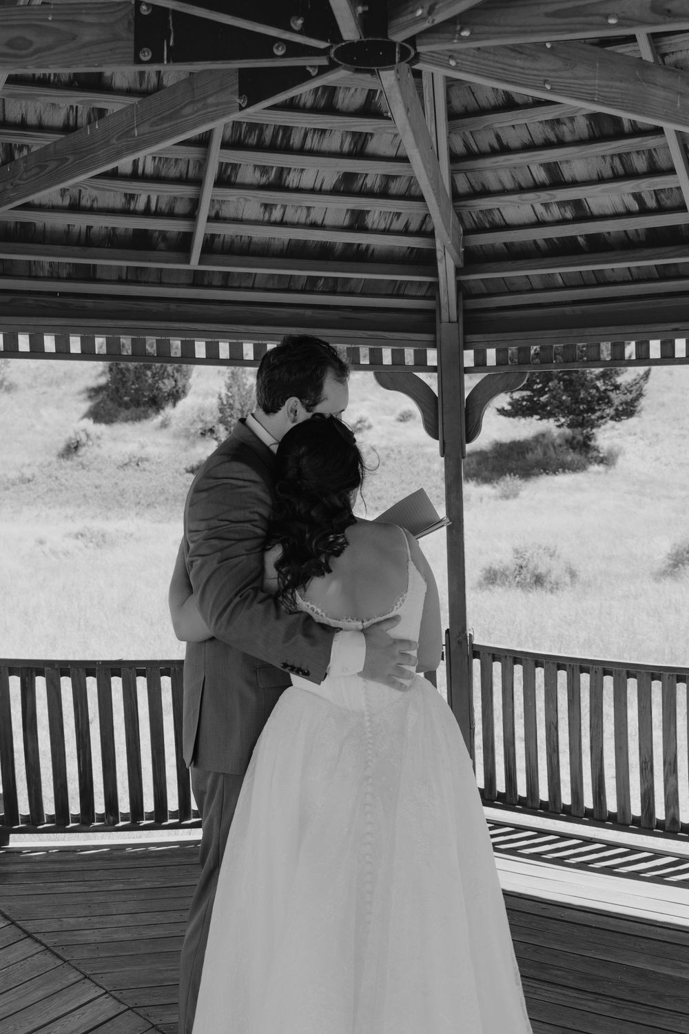 Black and white photo of bride and groom sharing a kiss under a wooden gazebo on their wedding day.