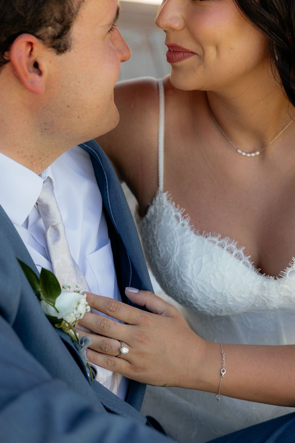 Close-up of bride and groom sharing an intimate moment, showcasing wedding rings, boutonniere, and elegant bridal gown.