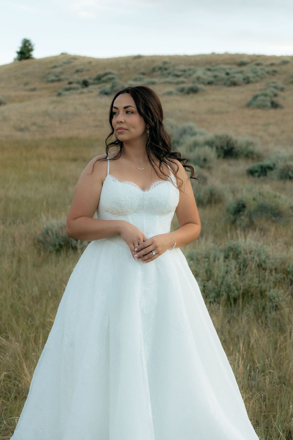 Bride in a white lace A-line wedding gown standing in a golden field with rolling hills behind her.