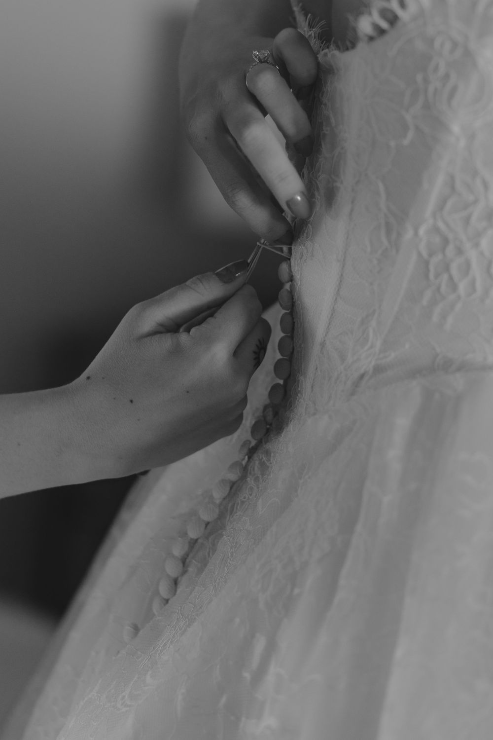 Hands fastening delicate lace buttons on a wedding dress in black and white photography.