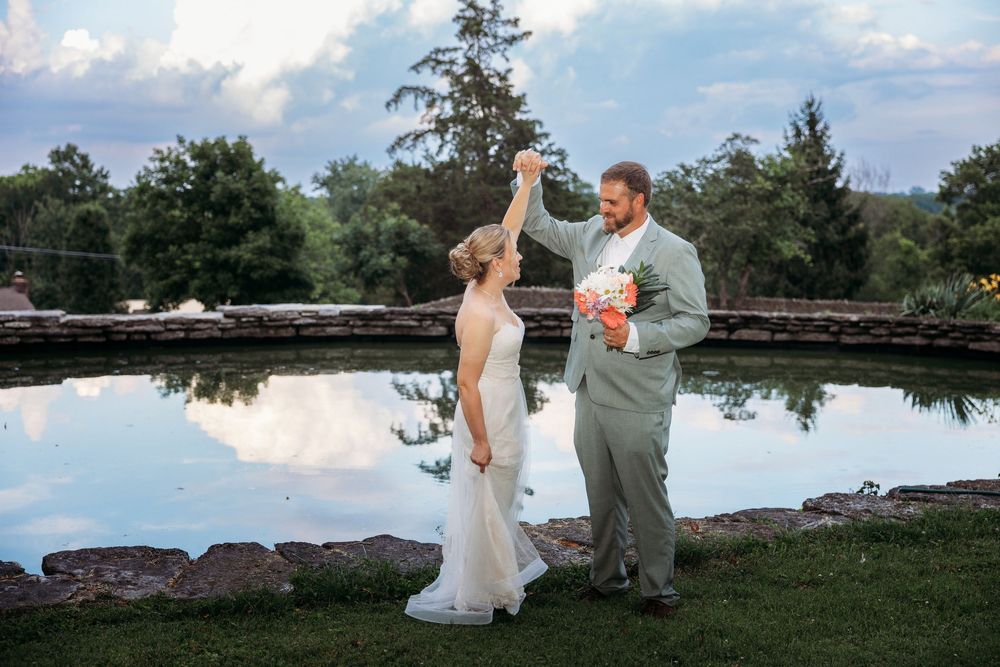 Bride and groom dancing outdoors near a reflective pond at a garden wedding ceremony at dusk.