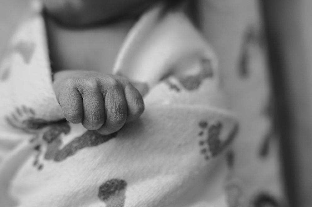 Close-up black and white photo of a newborn baby's tiny hand resting on a soft blanket with footprint pattern.