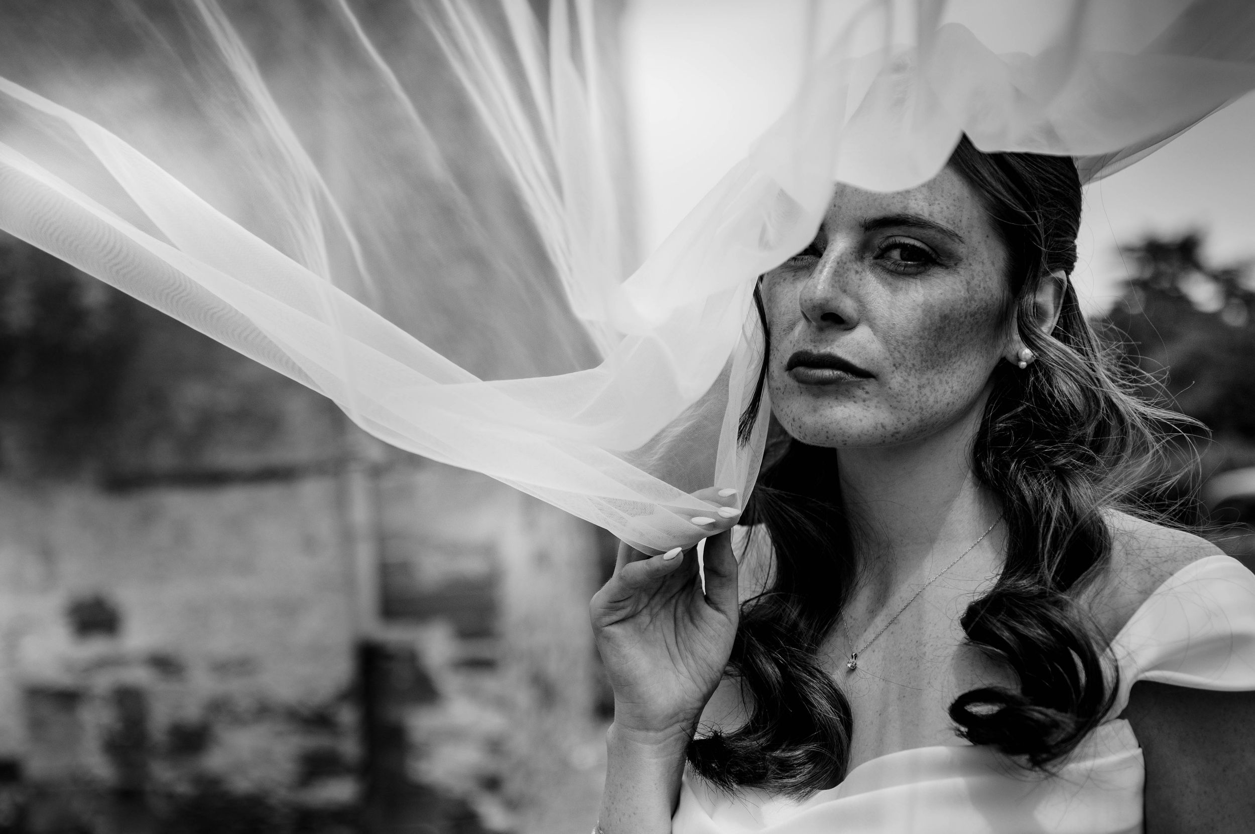 Portrait en noir et blanc de la mariée avec son voile flottant devant son visage.