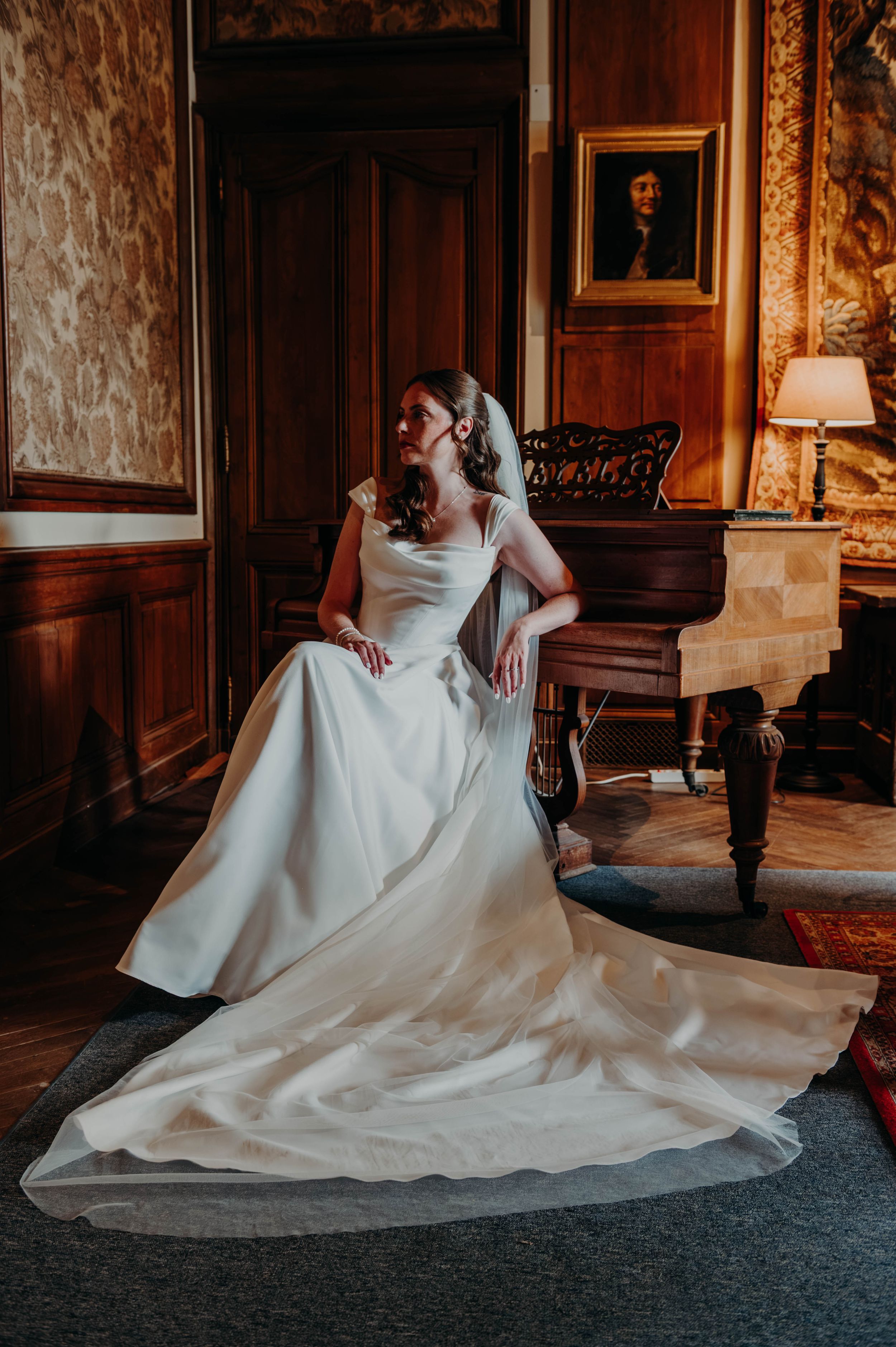 Portrait élégant de la mariée dans un salon ancien, avec sa robe et son voile déployés.