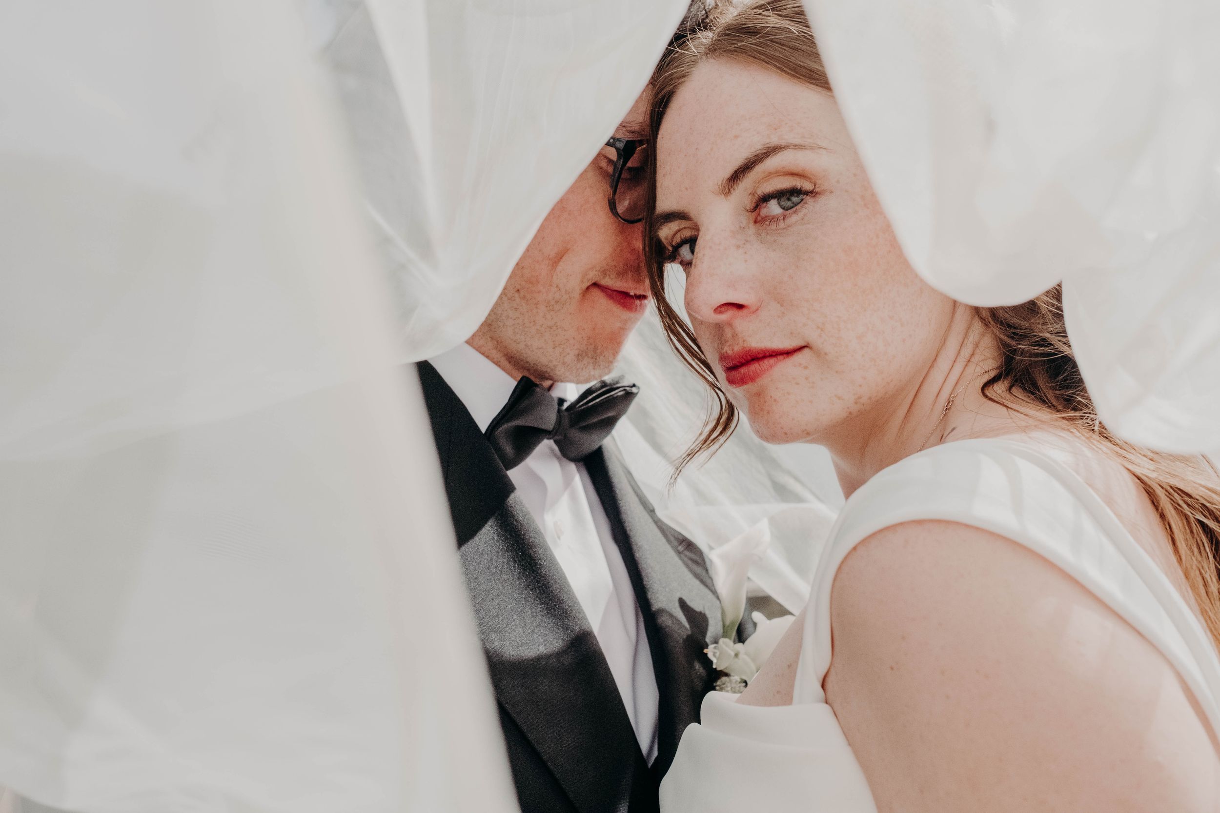 Portrait intime des mariés sous le voile de la mariée lors de leur séance photo de mariage.
