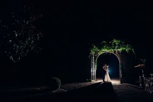 Silhouette des mariés de nuit sous une arche végétale éclairée.