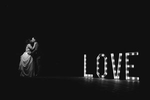 Photographie de mariage en noir et blanc avec les mariés enlacés près des lettres lumineuses LOVE.