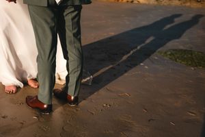 Détail des mariés marchant sur la plage, avec leurs tenues et leurs ombres sur le sable.