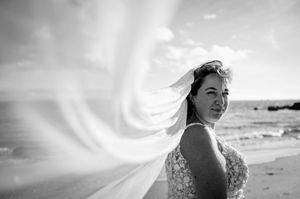 Portrait en noir et blanc d’une mariée sur la plage, son voile flottant dans le vent.