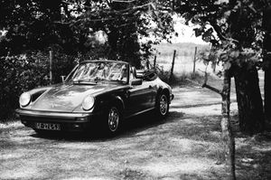 Voiture ancienne des mariés photographiée en noir et blanc sous les arbres.