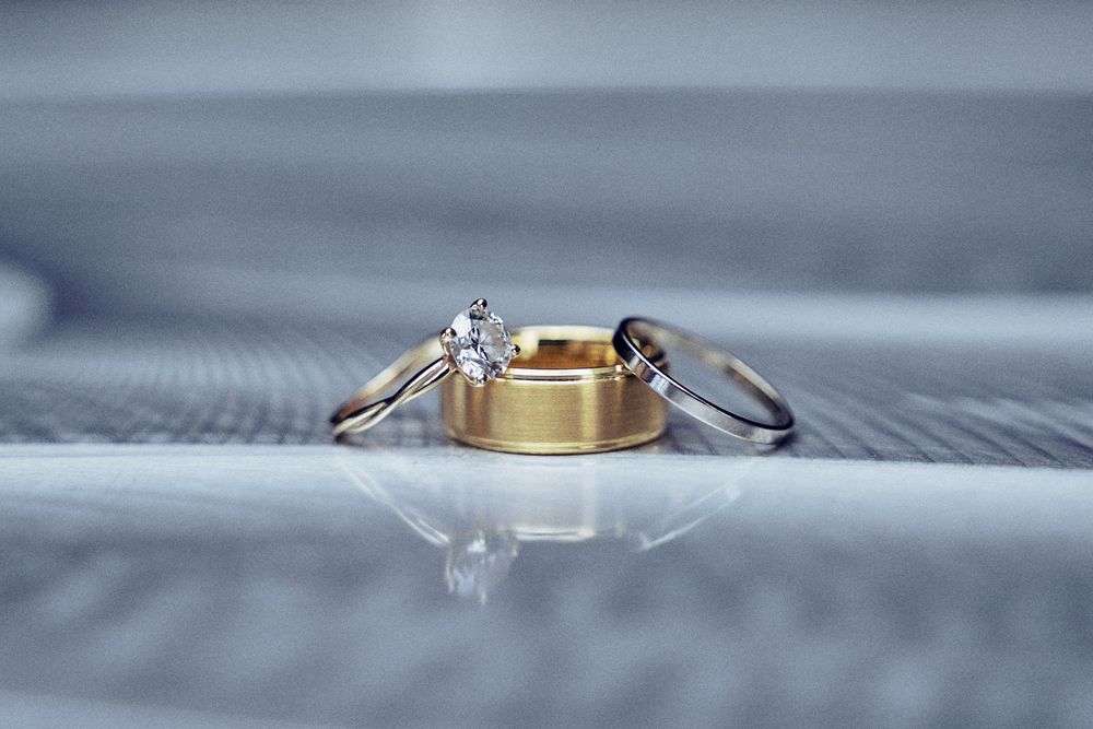 Three wedding rings, including a diamond engagement ring and gold band, displayed on a reflective surface.