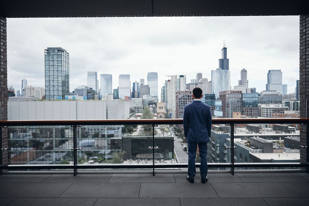 Businessman standing on urban balcony overlooking Chicago city skyline on overcast day.