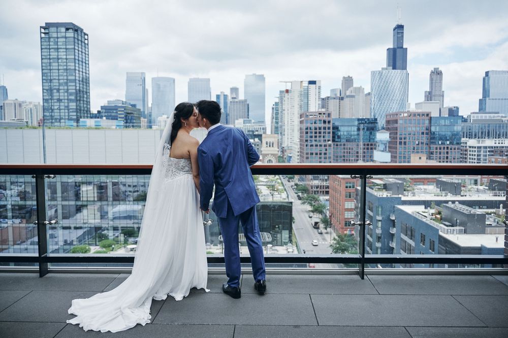 A newlywed couple shares a kiss on a rooftop terrace with the Chicago city skyline in the background.