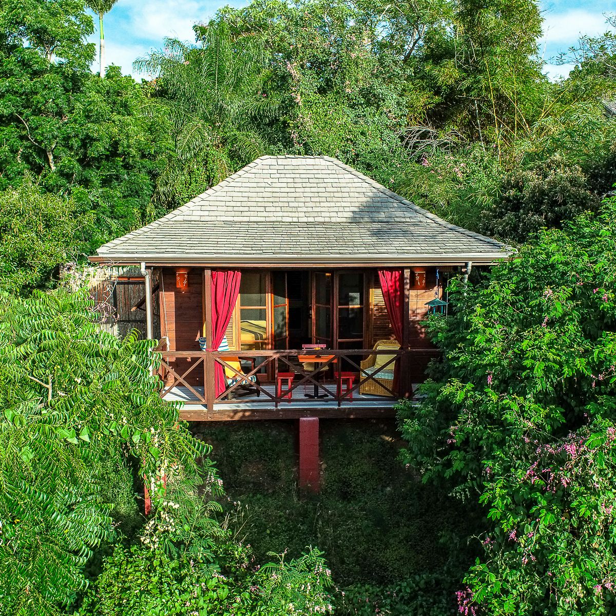Aerial view of a elevated tropical treehouse villa with red curtains surrounded by lush green jungle canopy.