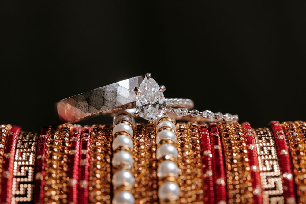 Diamond engagement ring and wedding band displayed on red and gold Indian bangles against dark background.