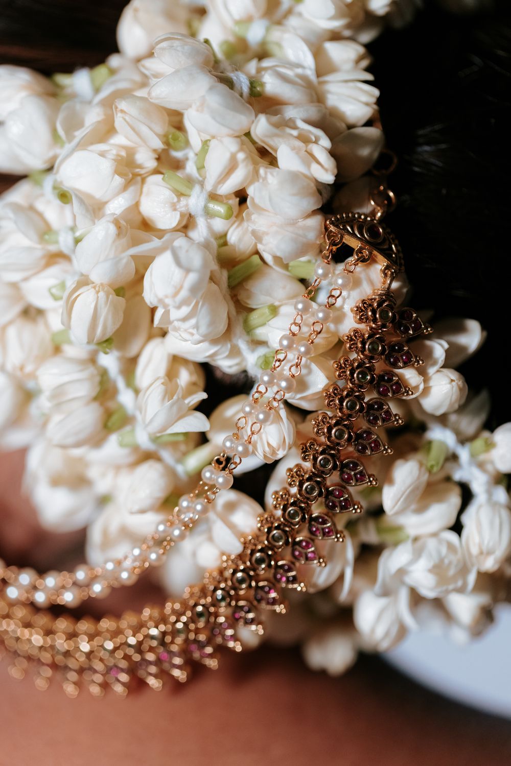 Gold and pearl bridal jewelry draped over white jasmine flowers, elegant wedding accessories close-up.