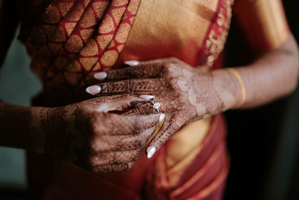 Close-up of intricate henna mehndi designs on bride's hands adjusting a red and gold sari.