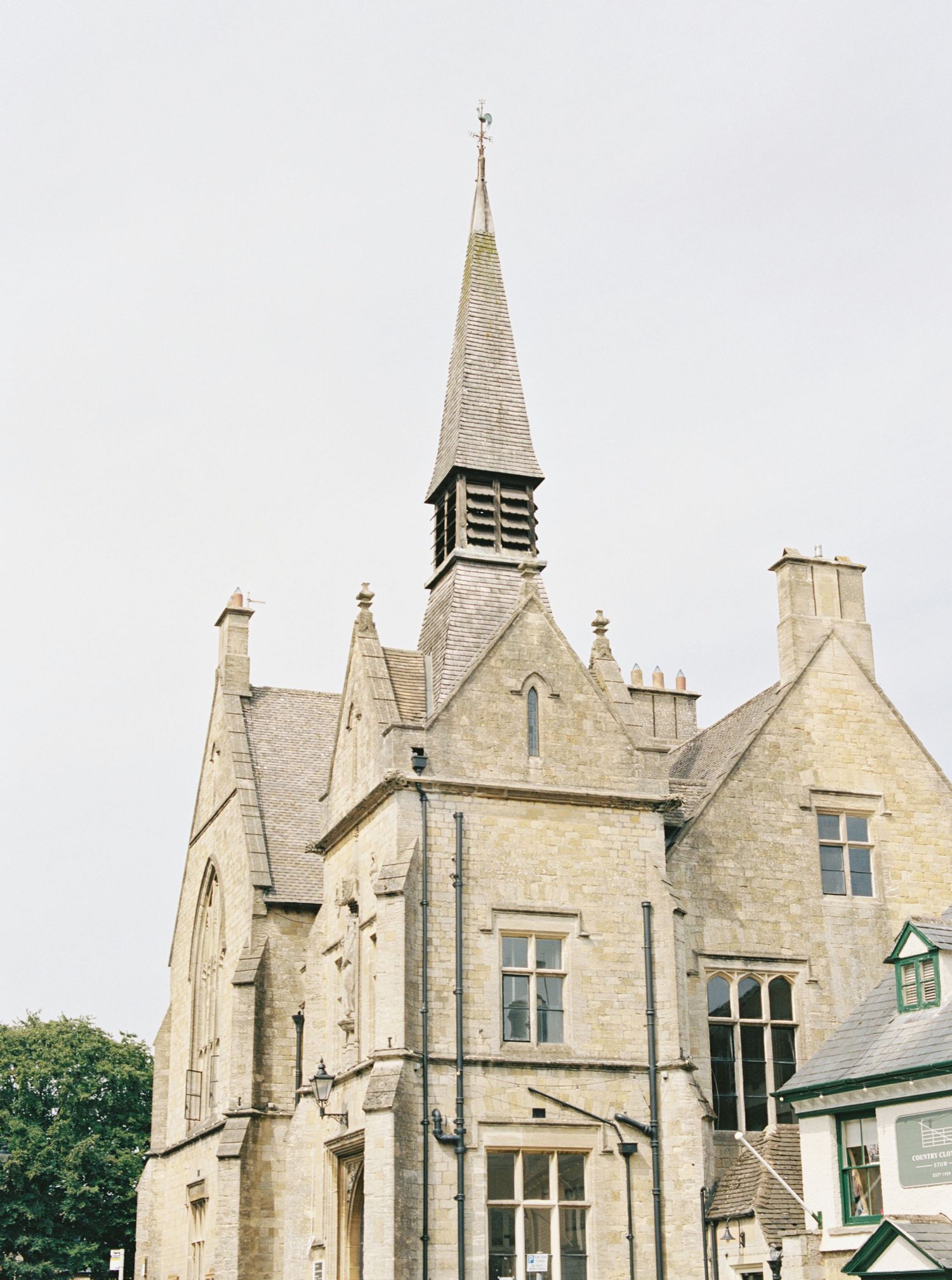 Historic stone church with Gothic spire and chimneys against overcast sky.