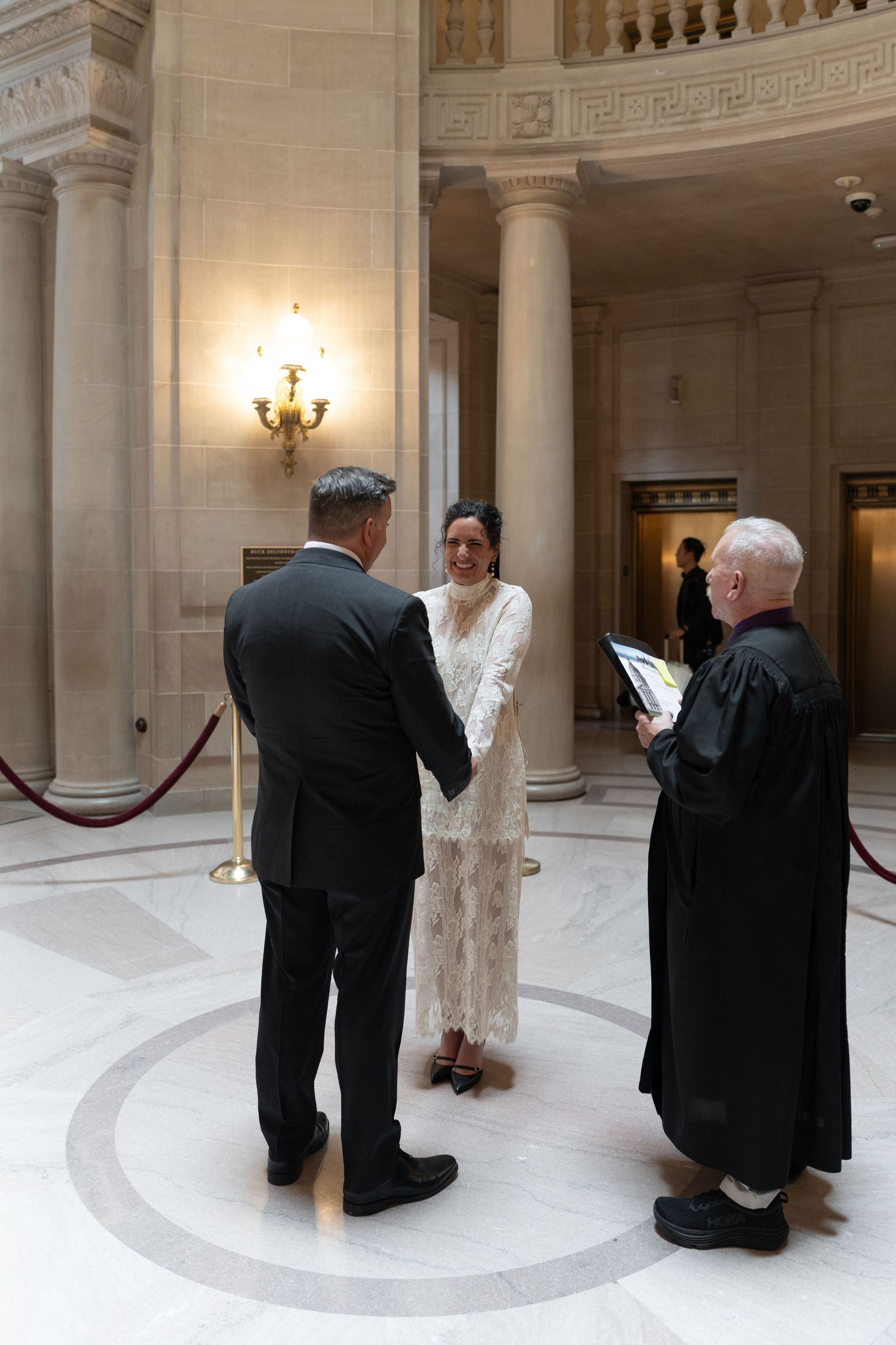 Couple exchanging vows in elegant courthouse rotunda with officiating judge, marble columns, and ornate architecture.