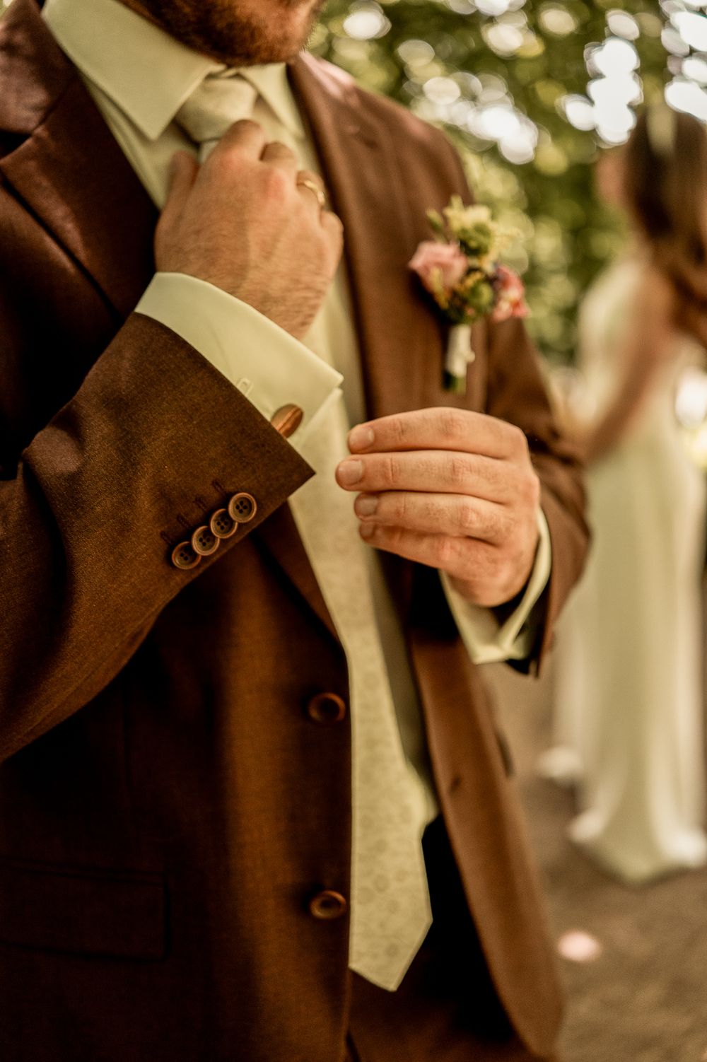 Nahaufnahme der Hochzeitsvorbereitungen: Der Bräutigam im braunen Anzug rückt seine Krawatte zurecht.