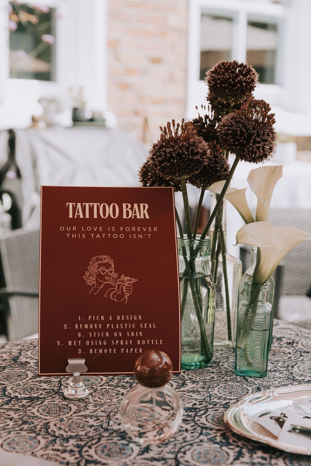 Elegant wedding tattoo bar sign on decorated table with dried allium flowers and white calla lilies in glass vases.