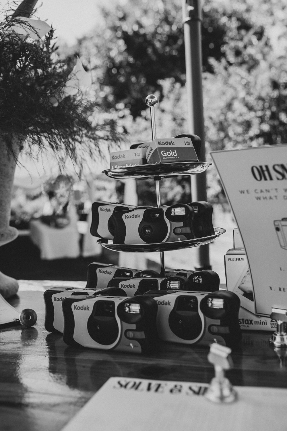 Black and white photo of Kodak disposable cameras stacked on a tiered display at a wedding reception.