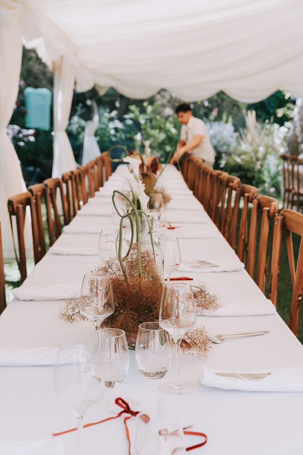 Elegant wedding reception table set with white linens, crystal glasses, and dried floral centerpieces under a marquee tent.